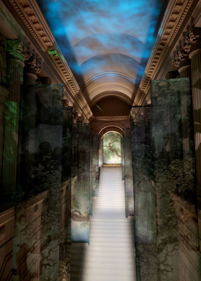 Light streams through a ceiling, casting shadows in a hallway with classical architecture and mural-covered walls
