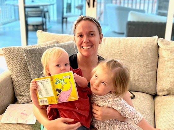 Elliott Walker with her two kids sitting on a couch and holding a book.