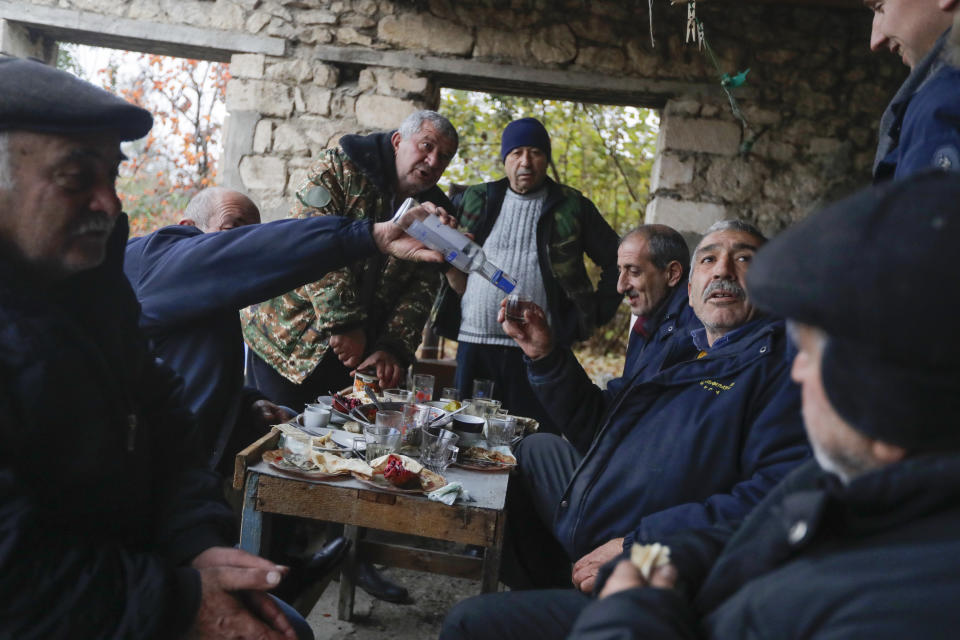 Ethnic Armenians drink vodka during their last dinner before leaving their homes in the village of Maraga, in the Martakert area, in the separatist region of Nagorno-Karabakh, Wednesday, Nov. 18, 2020. A Russia-brokered cease-fire to halt six weeks of fighting over Nagorno-Karabakh stipulated that Armenia turn over control of some areas it holds outside the separatist territory's borders to Azerbaijan. Armenians are forced to leave their homes before the region is handed over to control by Azerbaijani forces. (AP Photo/Sergei Grits)