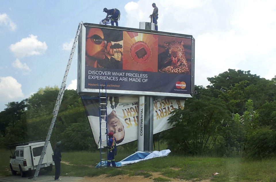 FILE - Workers take down a billboard of Olympic athlete Oscar Pistorius endorsing a product, bottom left, after Pistorius was taken into custody after Reeva Steenkamp, was shot dead at his home. Pistorius shot his girlfriend Reeva Steenkamp more than a decade ago in a Valentine's Day killing that jolted the world and shattered the image of a sports superstar.(AP Photo/Dion Chang-File)