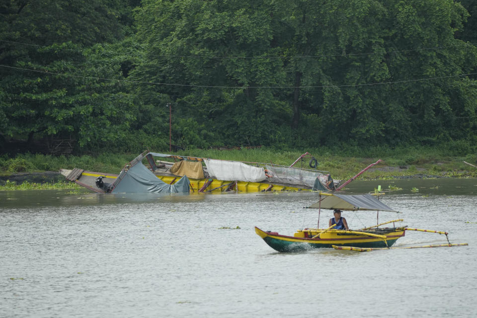 A man on his boat cruises near a capsized ferry in Binangonan, Rizal province, Philippines, Friday, July 28, 2023. The ferry turned upside down when passengers suddenly crowded to one side in panic as fierce winds pummeled the wooden vessel, killing a number of people, officials said Friday. (AP Photo/Aaron Favila)