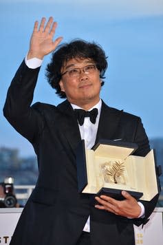 A man in a tuxedo waves and carries an award.