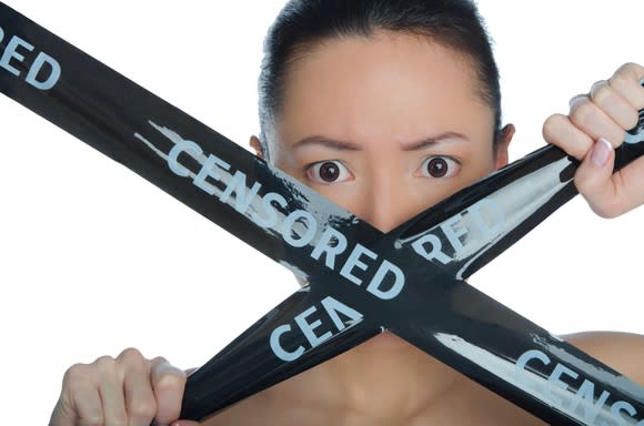 A woman holds a black ribbon reading "censored" across her mouth.