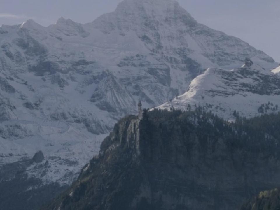 nurmen gard castle in fantastic beasts the crimes of grindelwald. a shot of a castle situated on a cliff, with tall mountains surrounding it