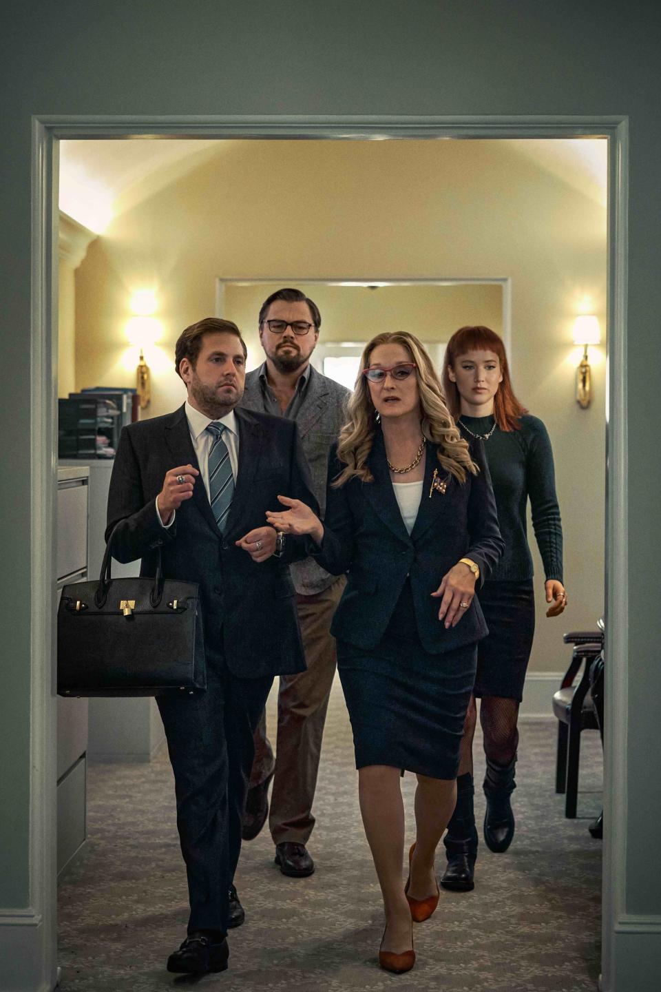 Meryl's character walking through a hallway as Jonah, who's holding her purse, follows along with Leo and Jennifer