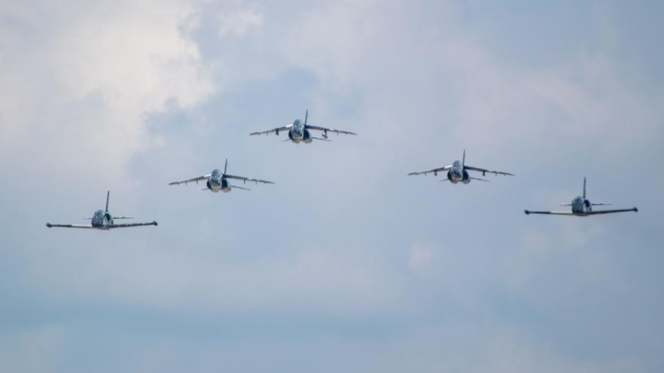 Fünf Jets fliegen in Formation am blauen Himmel.