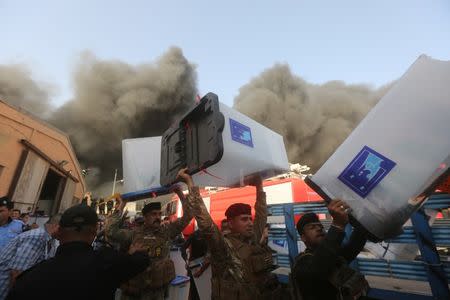 Security forces carry ballot boxes as smoke rises from a storage site in Baghdad, housing the boxes from Iraq's May parliamentary election, Iraq June 10, 2018. REUTERS/Stringer