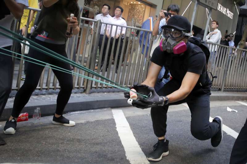 香港抗爭者11日以彈弓發射石塊。（美聯社）