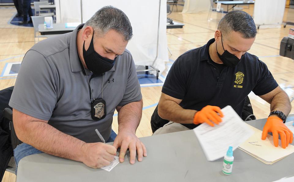 Milford Police Detective Mike Mastroianni, left, fills out forms for the COVID-19 vaccine, with Milford Police Sgt. Robert Tusino, who is also the department’s paramedic, at the Franklin High School gymnasium, Jan. 13, 2021.