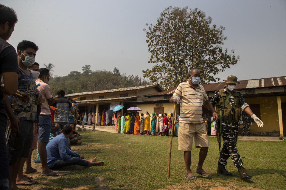 An Indian paramilitary person assists an elderly voter as people stand in queue to cast their votes in a polling station during the third phase of assembly election in Gauhati, India, Tuesday, April 6, 2021. Voters in four Indian states and a union territory are casting their ballots, in elections seen as a test for Prime Minister Narendra Modi’s government which is battling the latest surge in coronavirus cases. (AP Photo/Anupam Nath)