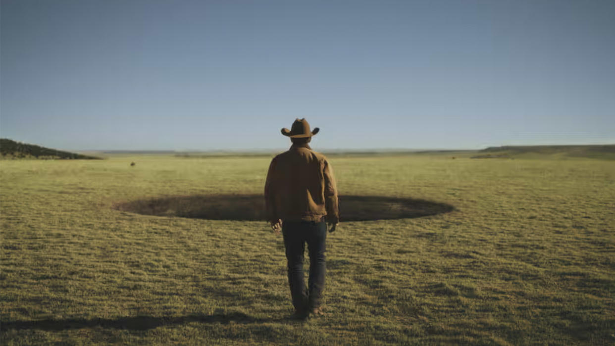  A lone cowboy walks towards a hole. 