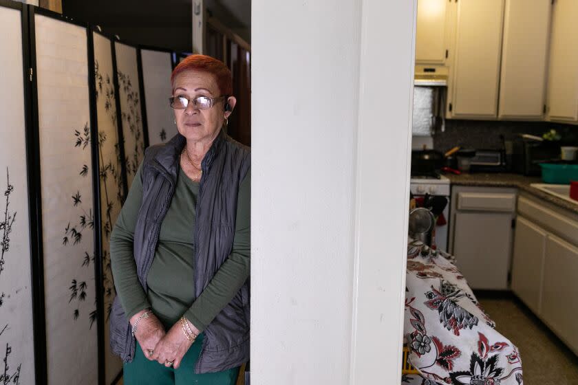 Panorama City, CA - April 05: Josephine Biclar, an elder care giver stands in the front entrance of her studio apartment that is divided by screens and makeshift walls on Wednesday, April 5, 2023 in Panorama City, CA. Biclar, shares a studio apartment with two other caregivers who are all 70 or older. (Jason Armond / Los Angeles Times)