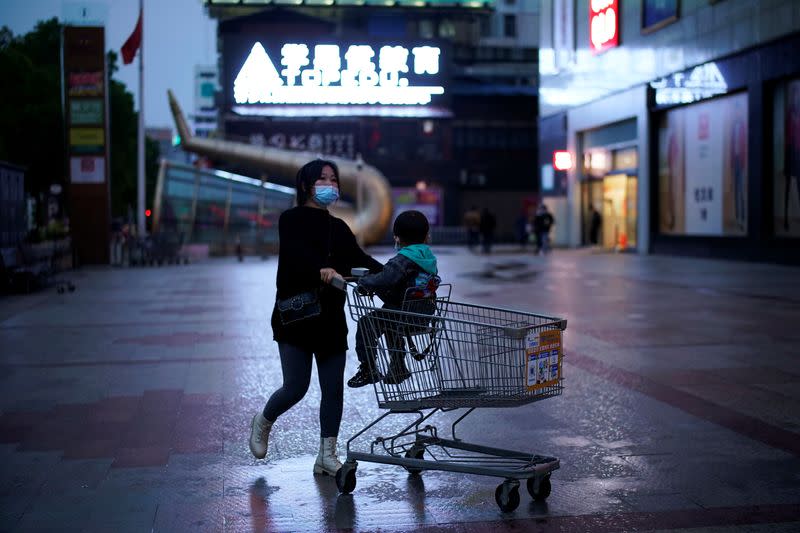 Woman wearing a face mask pushes a shopping trolley with a child sitting on it outside a shopping mall in Xianning