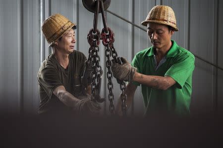 Workers wrap metal chains around steel bars to be transported at warehouse of the Baifeng Iron and Steel Corporation in Tangshan in China's Hebei Province August 3, 2015. REUTERS/Damir Sagolj