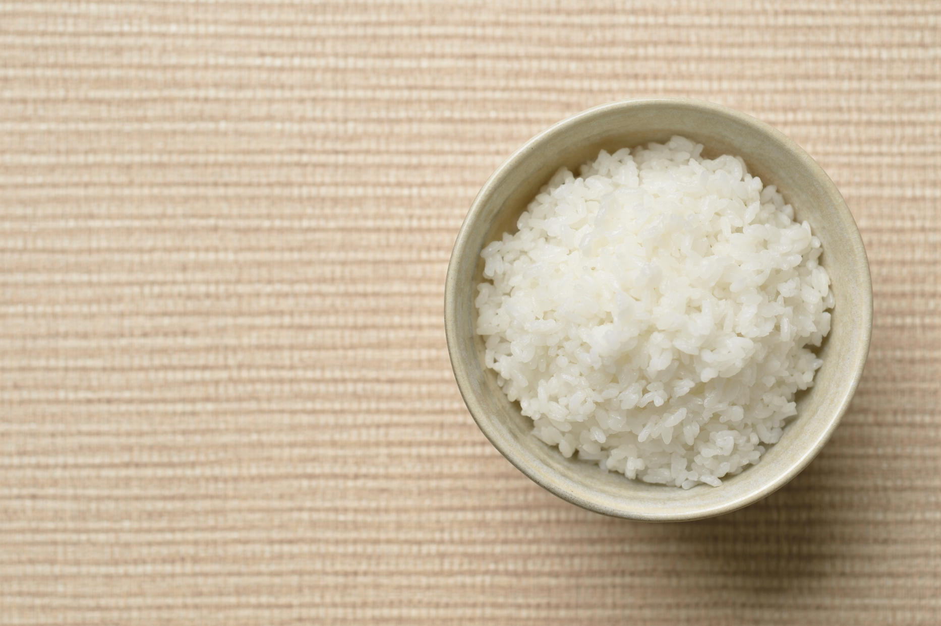 A bowl of rice is seen on a brown mat. Cooked rice unrefrigerated can cause food poisoning. 