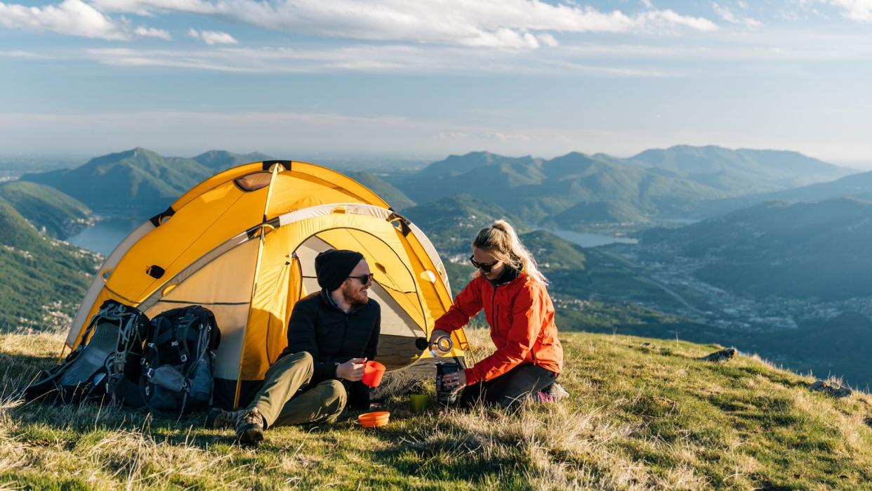  Man and woman sitting outside their tent outside in the sun. 