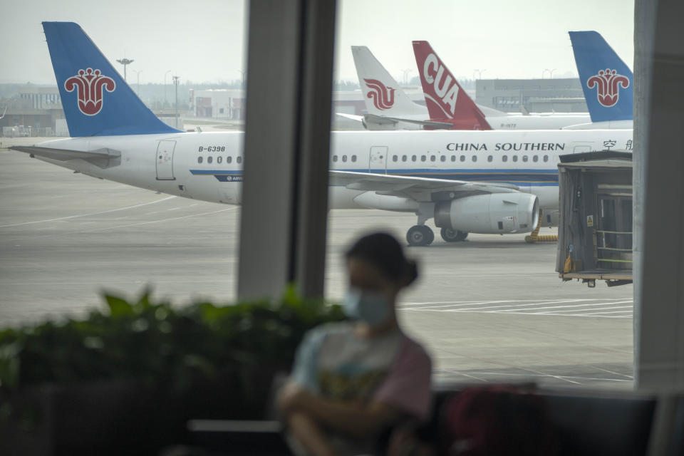 A traveler wearing a face mask sits in a concourse near parked jetliners from China Southern, China United, and Air China at Beijing Daxing International Airport in Beijing, Sunday, May 28, 2023. China's first domestically made passenger jet flew its maiden commercial flight on Sunday, as China looks to compete with industry giants such as Boeing and Airbus in the global aircraft market. (AP Photo/Mark Schiefelbein)