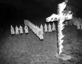 <p>Members of the Ku Klux Klan, wearing traditional white hoods and robes, stand back and watch with their arms crossed after burning a 15-foot cross at Tampa, Fla., Jan. 30, 1939. (Photo: AP) </p>
