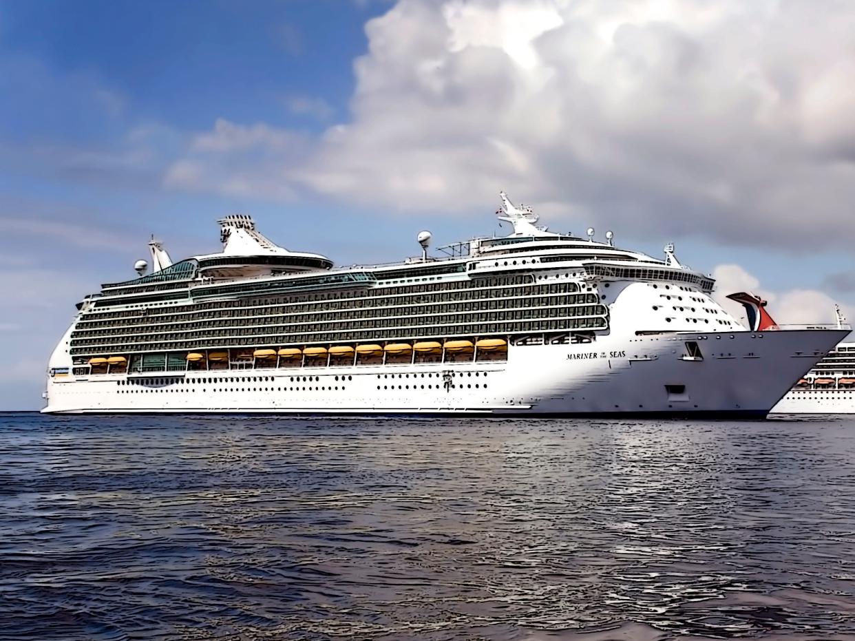 A large cruise ship with multiple stories and lifeboats on the side anchored off the coast of an island.