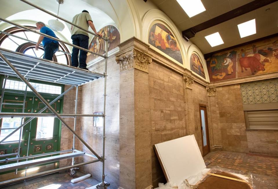 Art conservator Arthur Page and Tom Heffelfinger hang the painting “Fruit Picking” by Ray Boynton at the El Viejo Building, the former downtown Post Office, in Modesto, Calif., on Friday, July 22, 2022. The oil on masonite painting was one of nine murals commissioned during the 1930’s era arts program.