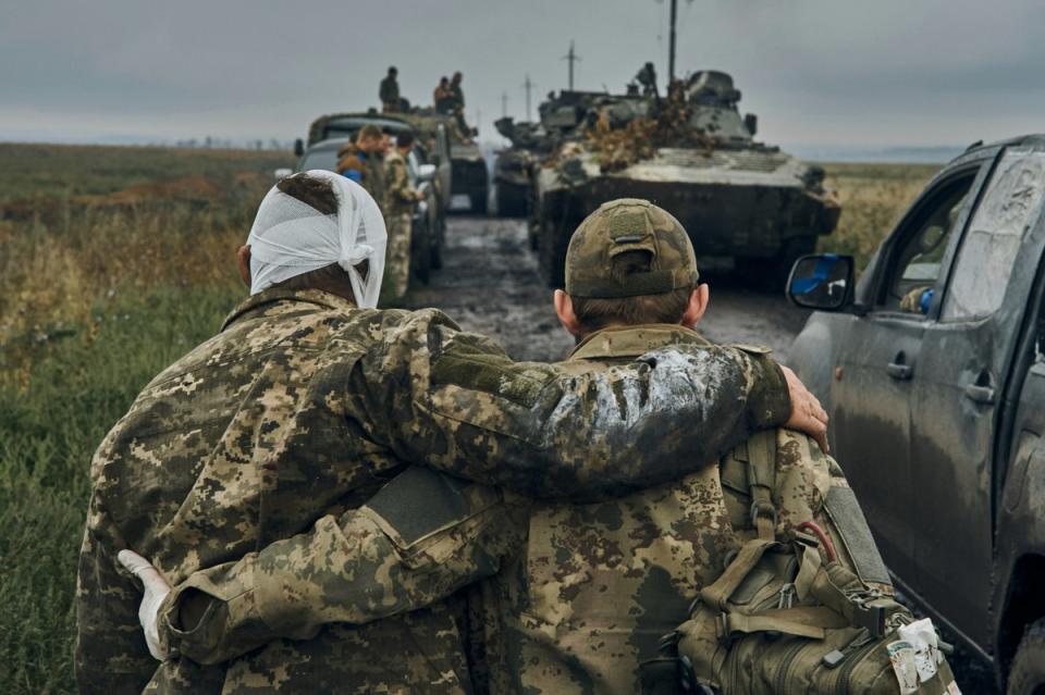 A  Ukrainian soldier helps a wounded fellow soldier on the road in the freed territory in the Kharkiv region (AP)