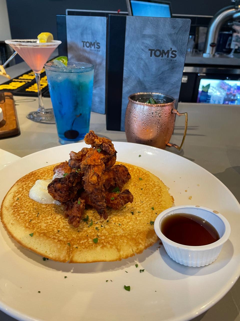 Tom's Crispy Chicken and Cornbread Pancake with pickle brined and hand-battered premium crispy chicken tenders, or tossed in Nashville hot sauce with honey butter and maple syrup.