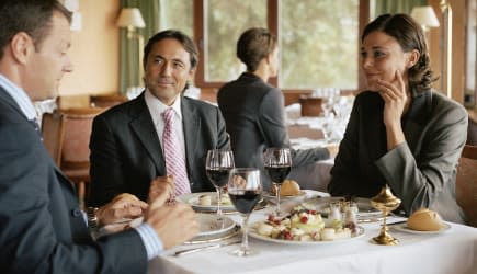 Two businessmen and woman at restaurant table, smiling
