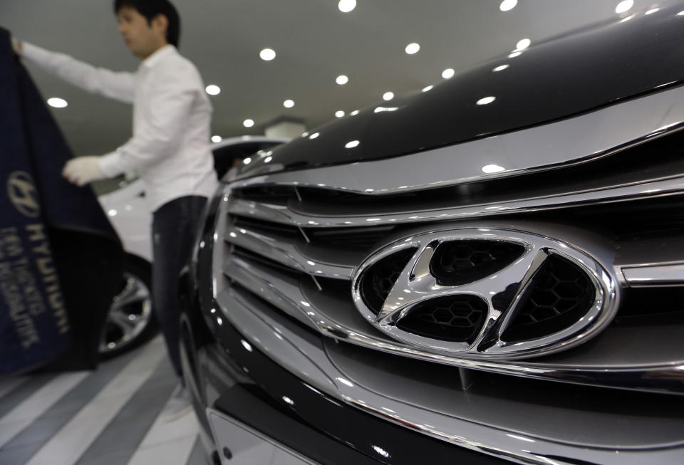 A man removes a carpet to clean near a Hyundai Motor's car on display at the company's showroom in Seoul, South Korea, Thursday, Oct. 25, 2012. Hyundai Motor Co. suffered a fall in third quarter profit versus the previous quarter after strikes dented vehicle production. (AP Photo/Lee Jin-man)