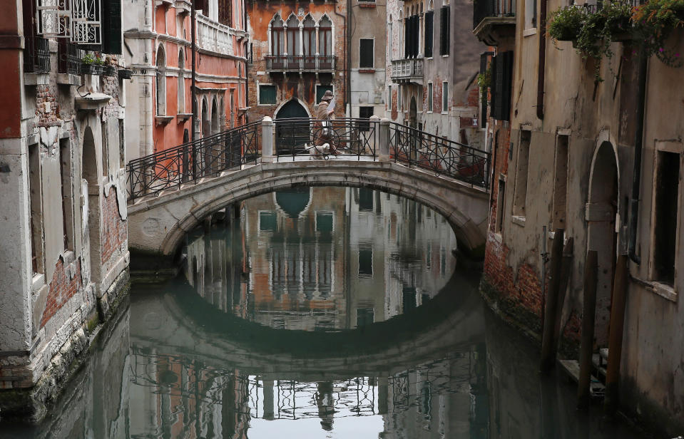 In this picture taken on Wednesday, May 13, 2020, a woman walks her dog in Venice, Italy. Venetians are rethinking their city in the quiet brought by the coronavirus pandemic. For years, the unbridled success of Venice's tourism industry threatened to ruin the things that made it an attractive destination to begin with. Now the pandemic has ground to a halt Italy’s most-visited city, stopped the flow of 3 billion euros in annual tourism-related revenue and devastated the city's economy. (AP Photo/Antonio Calanni)