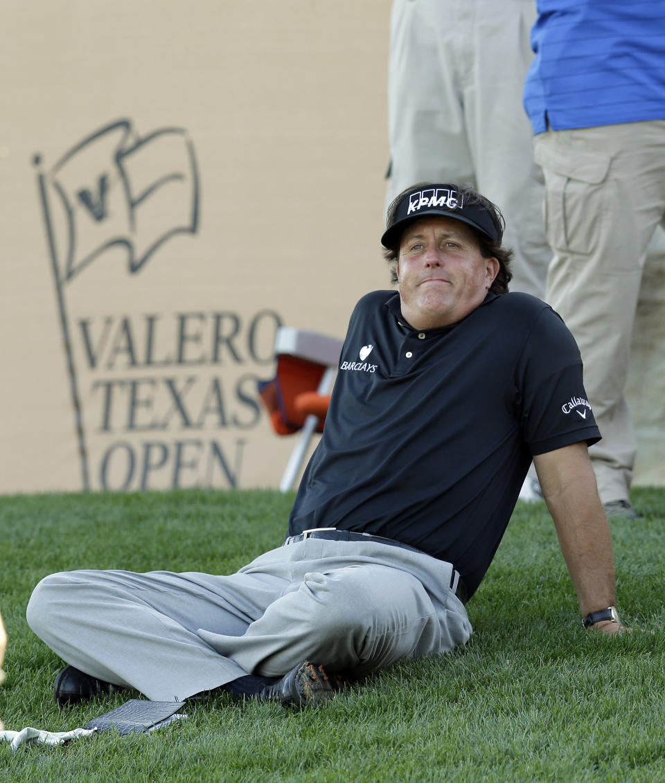 Phil Mickelson sits on the grass as watches his playing partners finish the 16th hole during the second round of the Texas Open golf tournament, Friday, March 28, 2014, in San Antonio. (AP Photo/Eric Gay)