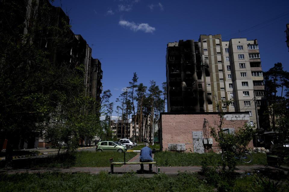 A resident sits outside buildings damaged by shelling in Irpin, outskirts of Kyiv, Ukraine, Tuesday, May 24, 2022. (AP Photo/Natacha Pisarenko)