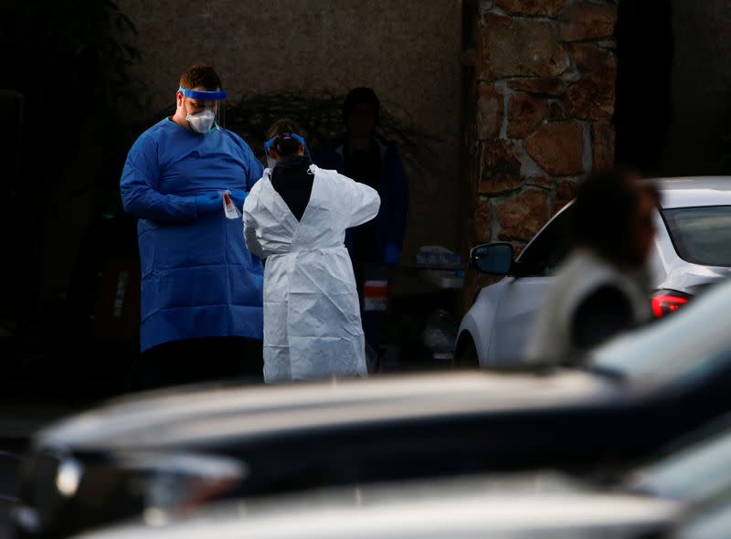 Nurses in protective gear handle a nasal swab sample as they test people in their vehicles outside Life Care Center of Kirkland