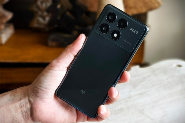 Person holding POCO X6 Pro in hand in front of tiny decorative wooden Christmas trees on a wooden table.