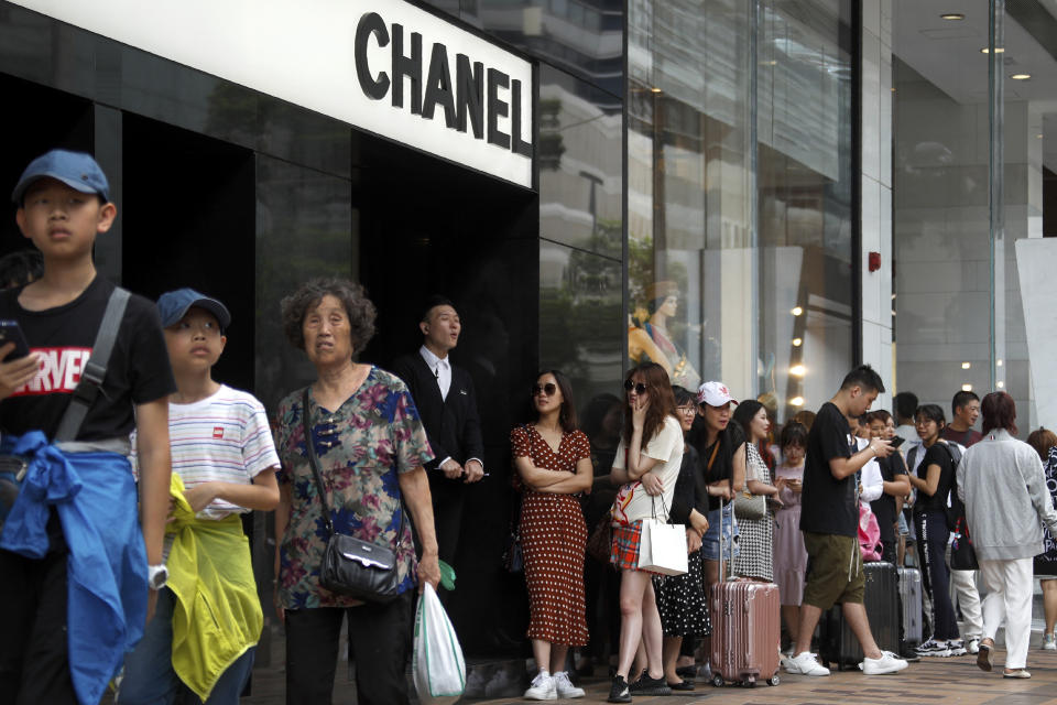 In this July 6, 2019, photo, tourists, some with their luggage line up to get into the Chanel store at the Canton Road, the one-stop-shop high street of high-end brands and popular with mainland Chinese tourists in Hong Kong. It's still the world's "freest" economy, one of the biggest global financial centers and a scenic haven for tycoons and tourists, but the waves of protests rocking Hong Kong are exposing strains unlikely to dissipate as communist-ruled Beijing's influence grows. (AP Photo/Andy Wong)