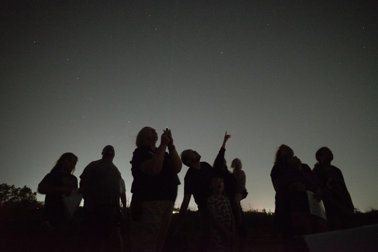 Curious stargazers follow the green laser beam from astronomer Brenda Colbertson as she points out the summer triangle cluster of stars during a guided viewing Aug. 26 at the top of Burnett's Mound at Skyline Park.