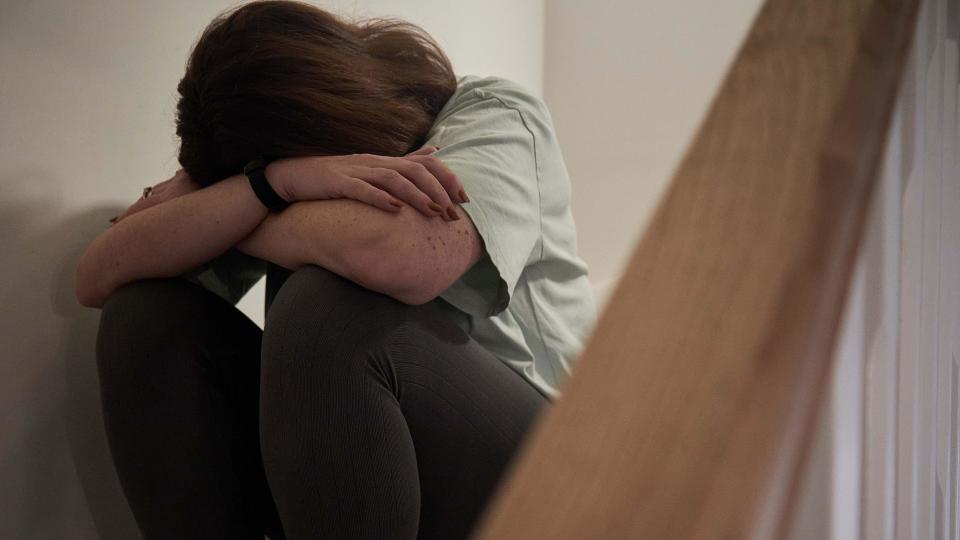 A woman sitting on the stairs at home. She's hiding her face. 