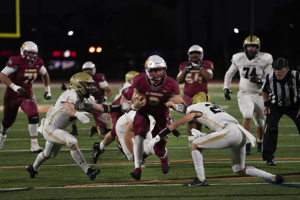 El Modena quarterback Jackson Keays, center, carries the ball against El Dorado during a high school football game in Orange, Calif., Friday, March 19, 2021. The team recently played its first football game in a year as more California counties ease coronavirus restrictions and life in the nation’s most populous state inches back to normalcy. (AP Photo/Jae C. Hong)