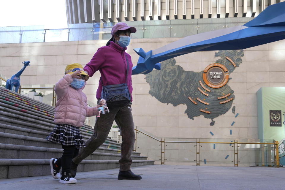 FILE - Residents wearing masks pass by a sign depicting Evergrande Group's China operation at one of their commercial projects in Beijing, China, Tuesday, Dec. 7, 2021. Financial markets can cope with the Chinese real estate developer that is struggling to avoid defaulting on $310 billion in debt, the central bank governor said Thursday, Dec. 9, 2021, in a new effort to assure the public the economy can be shielded from fallout. (AP Photo/Ng Han Guan, File)