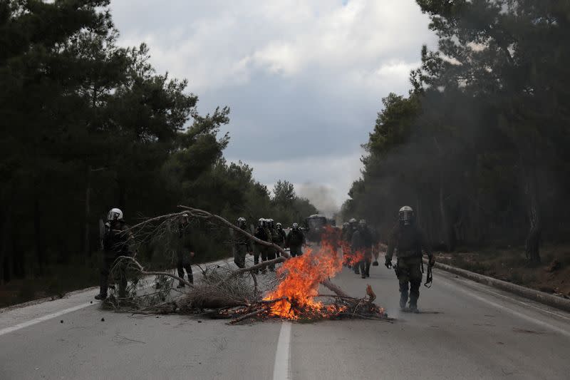 Riot police walk past burning tree branches as they clash with demonstrators, who oppose the building of a new closed migrant detention centre, in the area of Diavolorema on the island of Lesbos