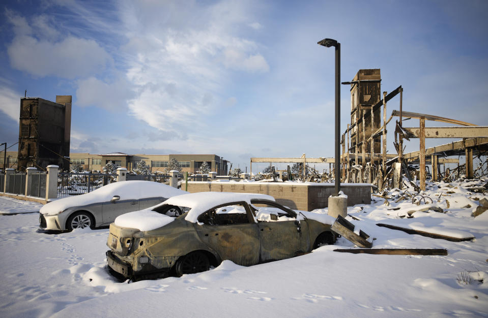 Snow left by a fast-moving winter storm is draped over the charred remains of a vehicle destroyed by wildfires in the parking lot of the Element hotel, which was also burned, Thursday, Jan. 6, 2022, in Superior, Colo. Colorado authorities said Thursday, that last week's wildfires caused $513 million in damage and destroyed 1,084 homes and structures. (AP Photo/David Zalubowski)