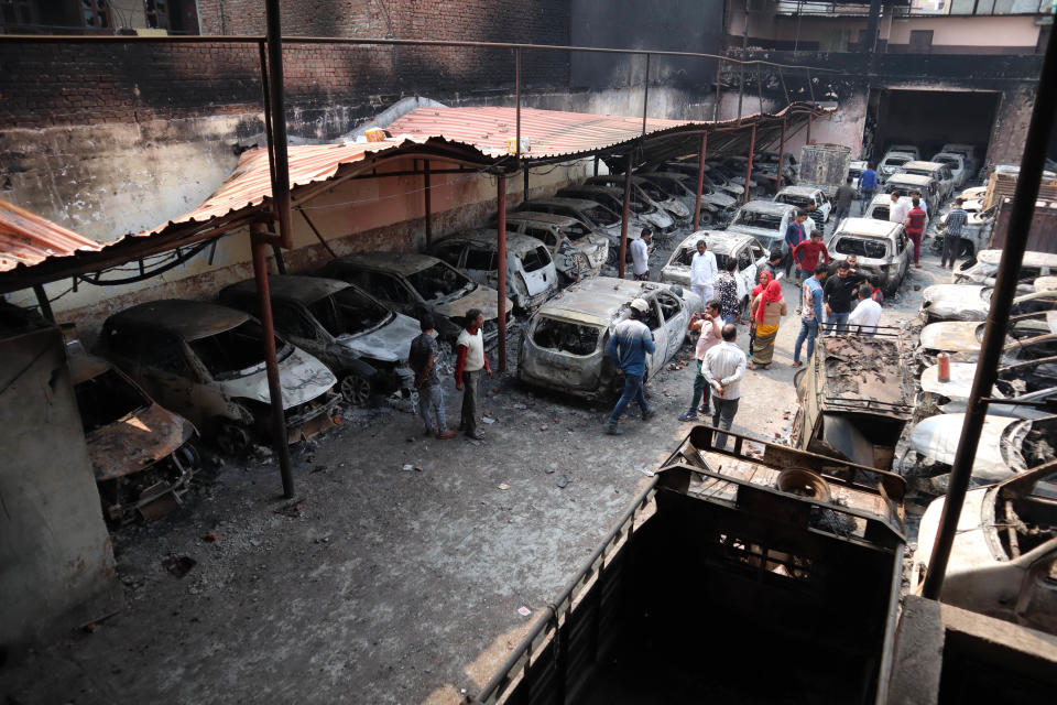 People walk besides burnt cars after a parking space was set on fire by a mob during riots in Chandbagh area of New Delhi on 29 February 2020. (Photo by Muzamil Mattoo/NurPhoto via Getty Images)