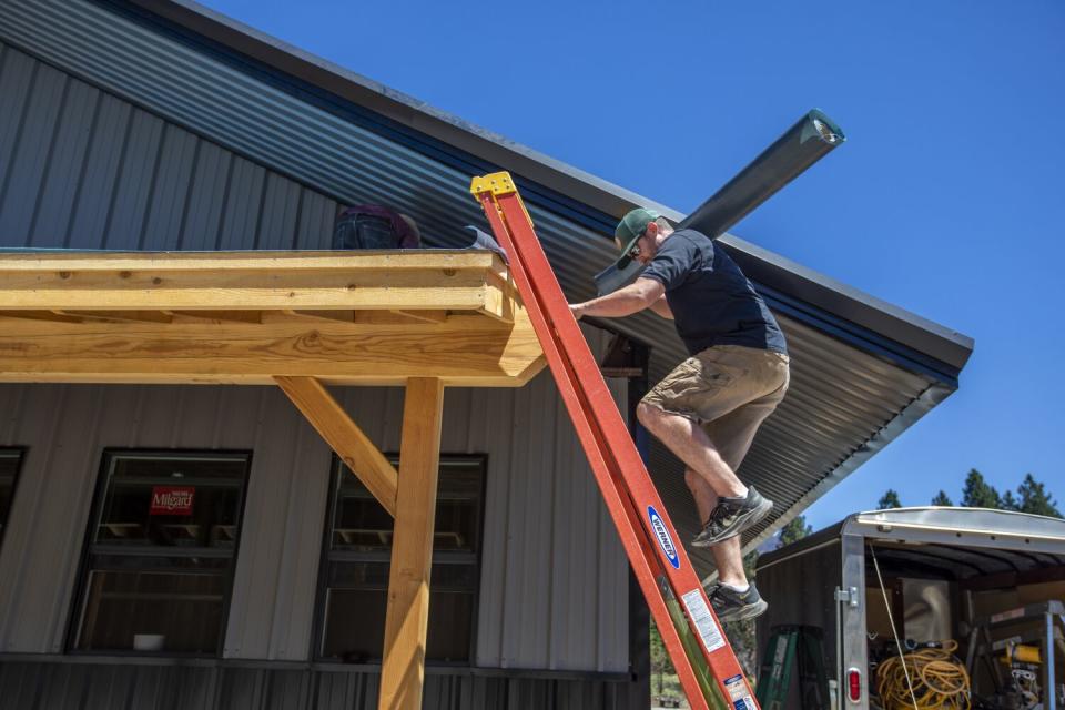 Kaley Bentz, owner of Riley's Jerky carries roofing tile up a ladder in Greenville.