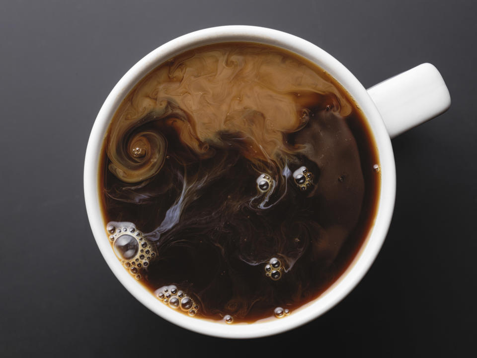 Top view of a cup of coffee with some cream inside swirling as it mixes