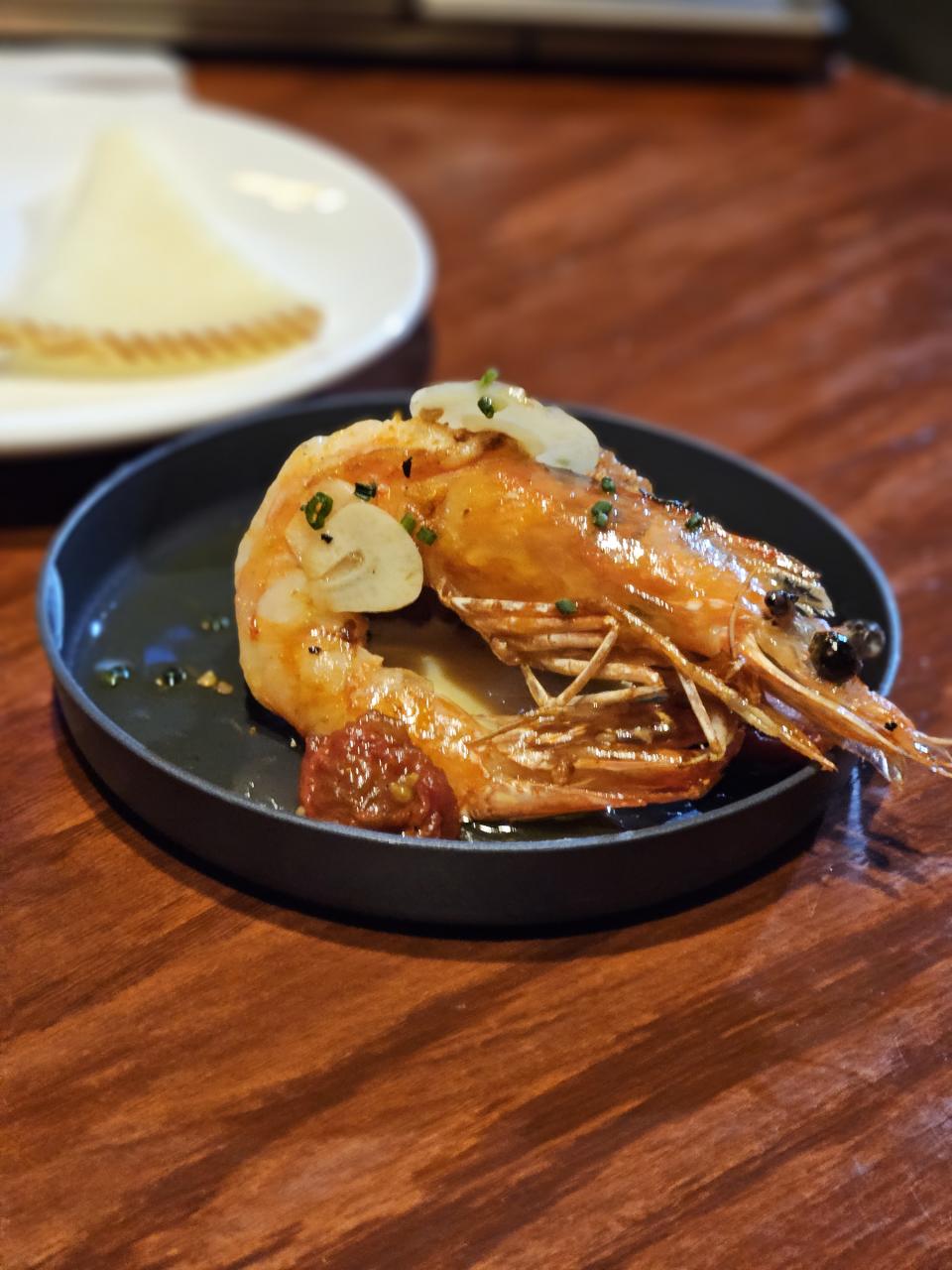 <p>Galaxy S23 Plus camera sample: A shiny sauteed shrimp with slices of garlic on it, placed on a black plate.</p>
