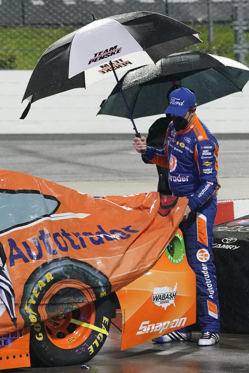 Brad Keselowski helps to cover his car during a rain delay at the NASCAR Cup Series auto race at Martinsville Speedway in Martinsville, Va., Saturday, April 10, 2021. (AP Photo/Steve Helber)