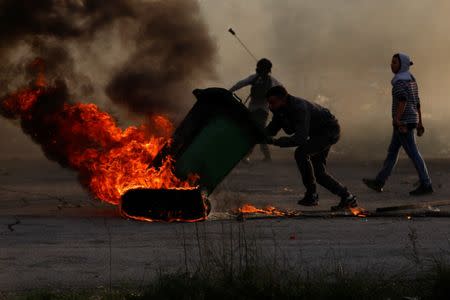 A Palestinian uses a trash container to move a burning tire during clashes with Israeli troops near the Jewish settlement of Beit El, near Ramallah, in the Israeli-occupied West Bank December 13, 2018. REUTERS/Mohamad Torokman