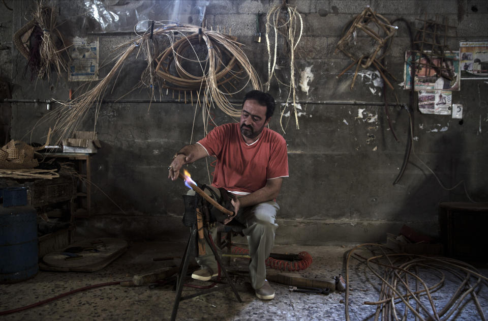 In this Saturday, July 6, 2019 photo, Palestinian Tarek Khalaf uses a flame to form bamboo at his family's workshop in Gaza City. Talk about old Gaza, and what pops up are images of clay pottery, colorful glassware, bamboo furniture and ancient frame looms weaving bright rugs and mats. As such professions could be dying worldwide, the pace of their declining is too fast in Gaza that out of its some 500 looms, only one is still functioning. (AP Photo/Khalil Hamra)