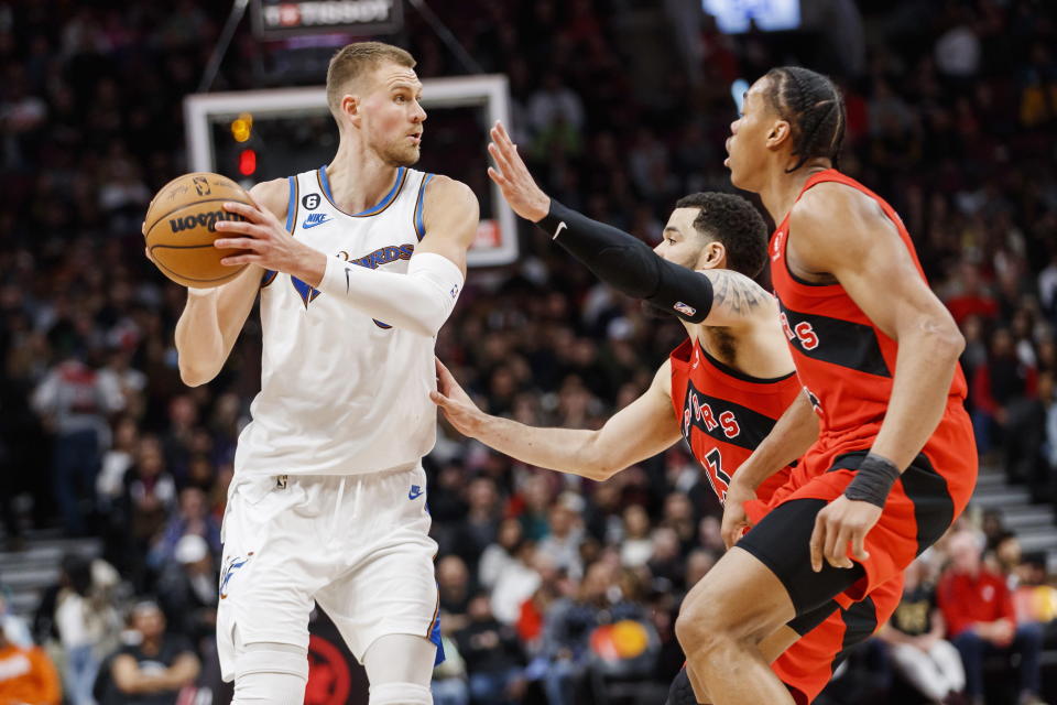 Washington Wizards center Kristaps Porzingis (6) is guarded by Toronto Raptors guard Fred VanVleet (23) and forward O.G. Anunoby (3) during the first half of an NBA basketball game in Toronto, Sunday, March 26, 2023. (Cole Burston/The Canadian Press via AP)