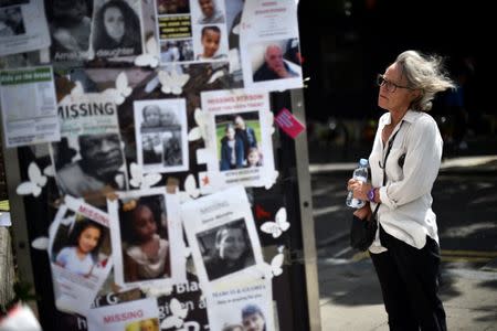 A woman looks at pictures of the victims of the fire at the Grenfell apartment tower stuck to a telephone box in North Kensington, London, Britain, June 23, 2017. REUTERS/Hannah McKay