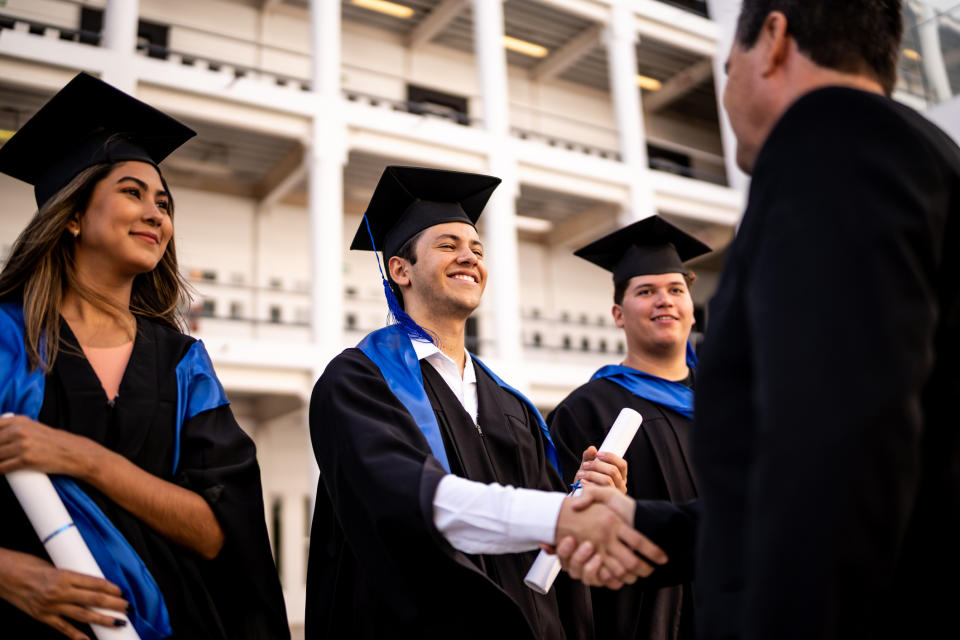 Graduates in cap and gown shaking hands with a faculty member at a graduation ceremony